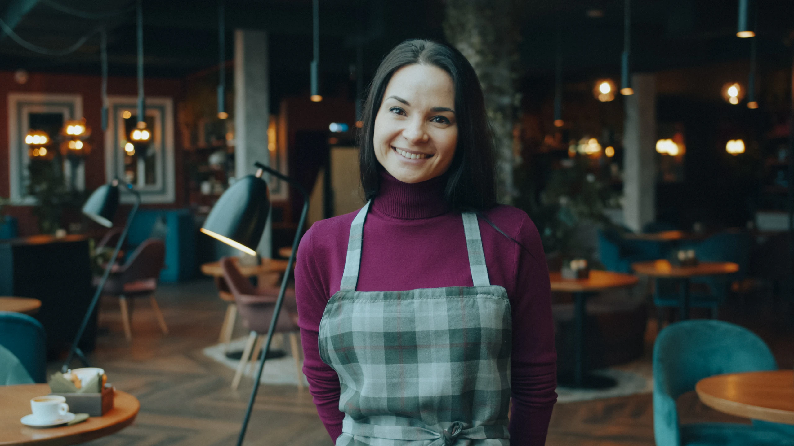 Cafébesitzerin in Schürze lächelt in ihrem warm beleuchteten Café