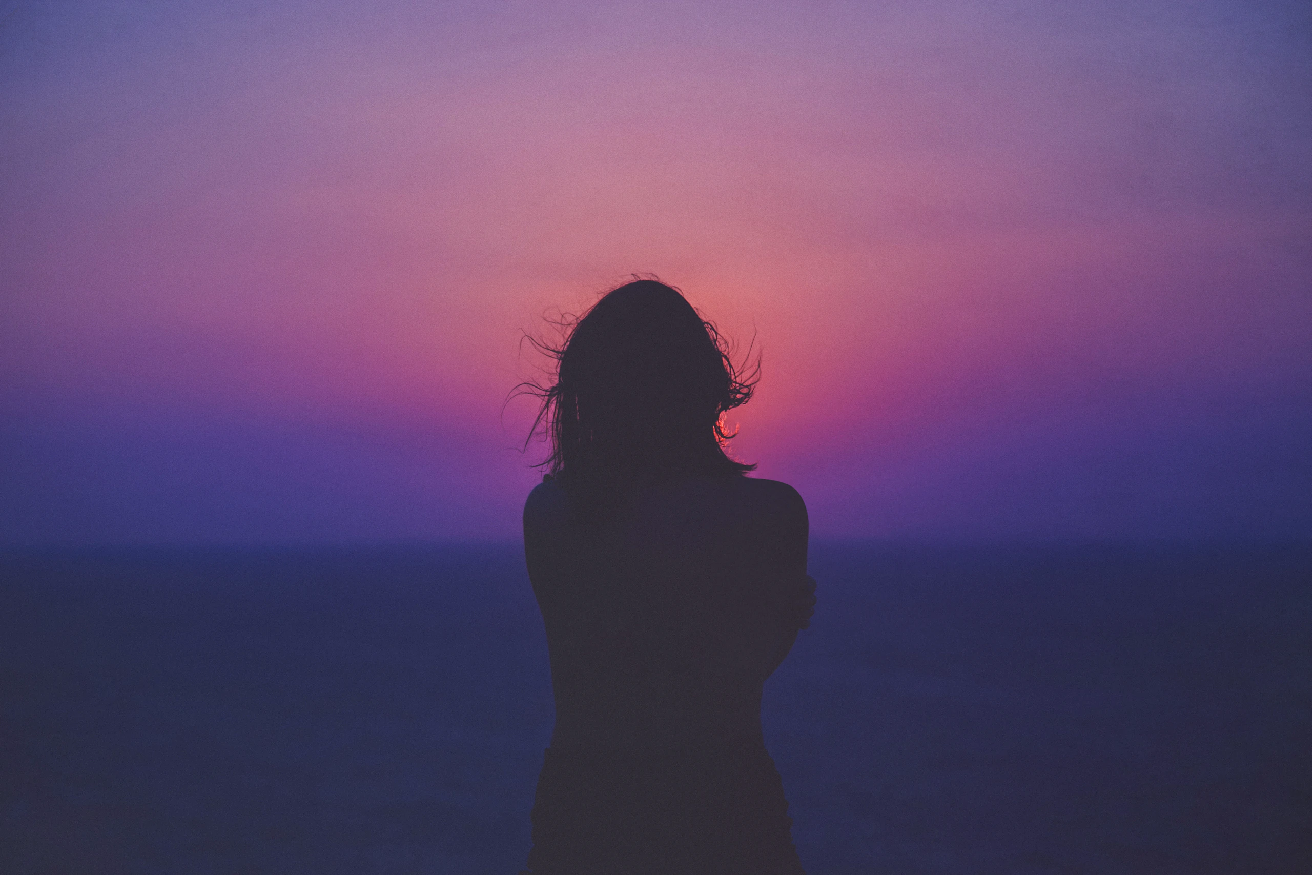 Silhouette einer Frau vor violett und rosa Abendhimmel